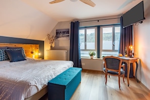 Ein Schlafzimmer mit einem Bett, einem Schreibtisch, einem Stuhl, einem Fenster mit Vorhängen und Blick ins Freie.