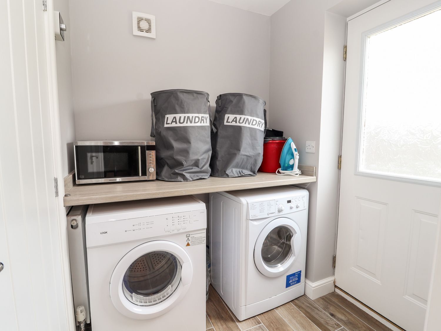 A laundry room with a washing machine, dryer, microwave, and two laundry bags on a shelf.