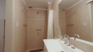 A modern bathroom with a walk-in shower, a white sink with multiple faucets, and a large mirror.