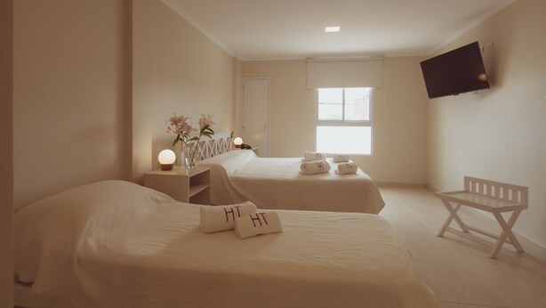 A hotel room with two beds, a TV mounted on the wall, a window, and a bench. - Hotel Tonight (Salta)