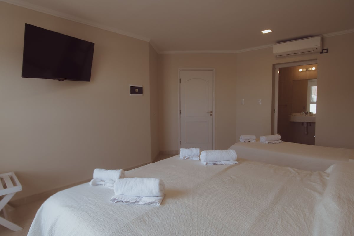 Ett hotellrum med två sängar, en platt-TV som är monterad på väggen, en dörr och en luftkonditioneringsanläggning.