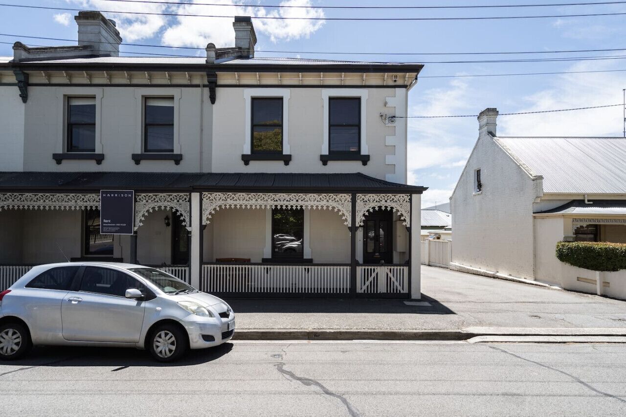 Un bâtiment à deux étages, avec une façade blanche et des éléments décoratifs noirs. Une voiture est garée devant.