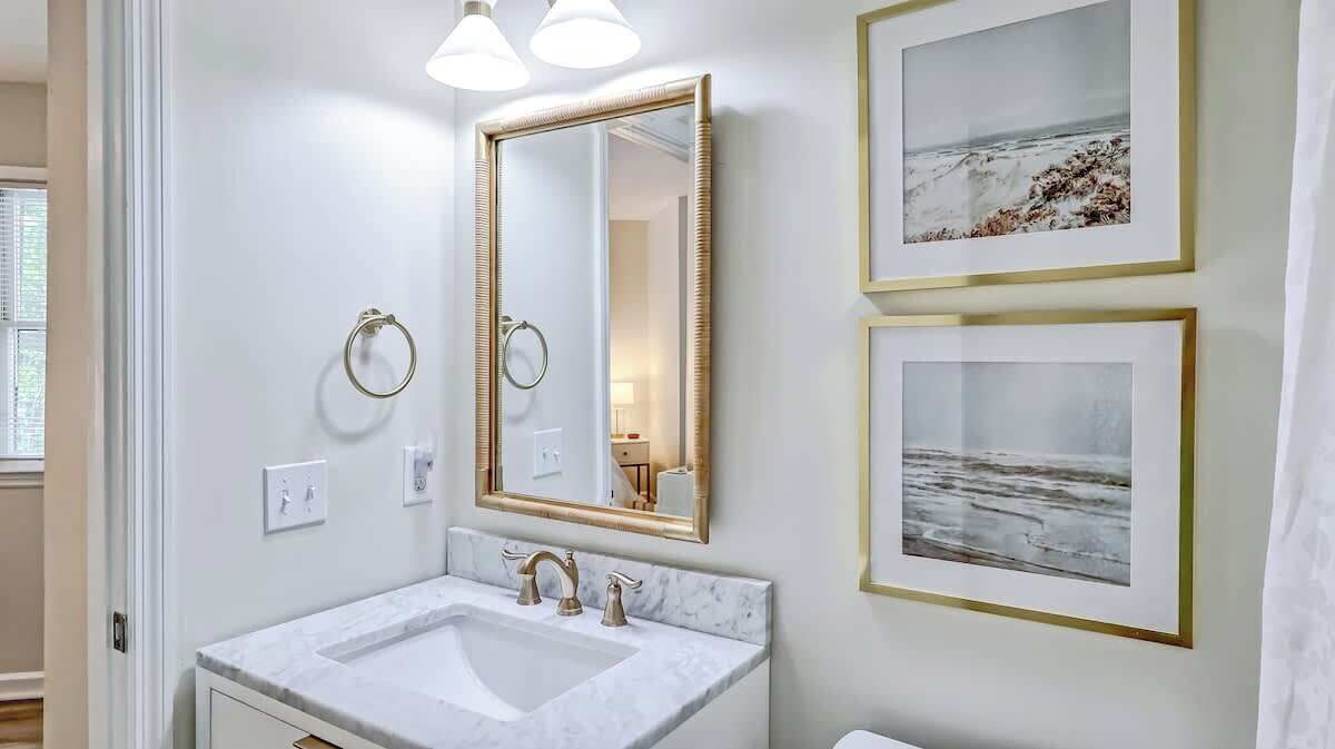 A bathroom with a white sink, gold-framed mirror, and two framed pictures on the wall.