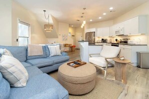 A modern living room with a sofa, ottoman, and a dining area with a table and chairs.