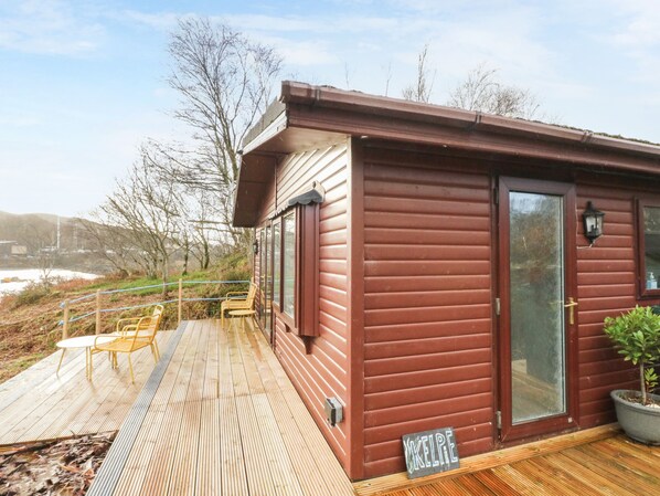 A wooden cabin with a deck, a sliding glass door, and a small outdoor seating area.