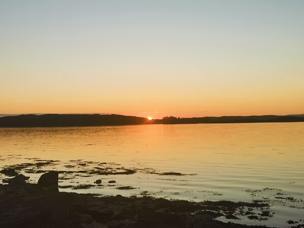 A sunset over a calm lake with a silhouette of a hill in the distance. - Kelpie (Lochgilphead)