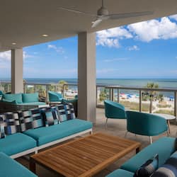 Relax in a spacious outdoor seating area with ocean and beach views, featuring comfortable sofas and armchairs.