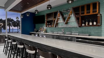 A bar area with a long counter, bar stools, and a large 'M' shaped shelf unit displaying bottles and glasses.