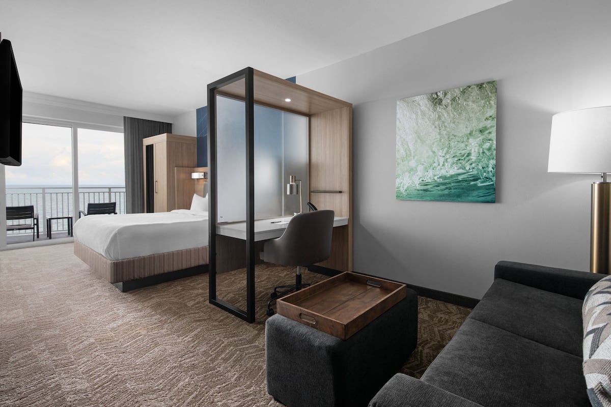 A modern hotel room with a bed, desk, and seating area.