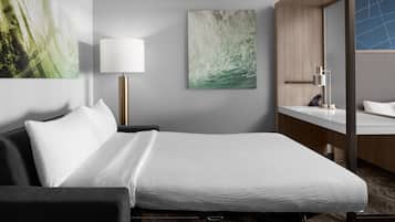 A hotel room with a bed, a bedside table with a lamp, a bathroom with a sink, and two wall-mounted paintings.