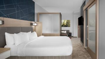 A modern hotel room with a large bed, a wooden headboard, a flat-screen TV, and a large window with a view of greenery.