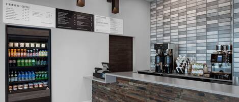 A modern coffee shop interior with a stone-textured counter, a beverage dispenser, and a menu board.