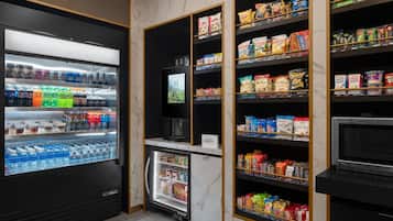 A self-service snack and beverage kiosk with refrigerated drinks, a coffee machine, and shelves stocked with snacks and packaged foods.