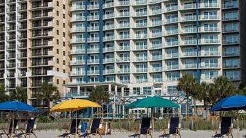 A beachfront hotel with multiple balconies, beach chairs, and umbrellas.