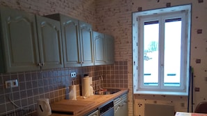 Une cuisine avec des meubles de couleur bleu clair, un plan de travail en bois, un lave-vaisselle et une fenêtre donnant sur l’extérieur.