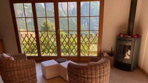 A cozy room with wicker furniture, a fireplace, and a view of a mountainous landscape through large glass doors. - Chalet - Calm, comfort and splendid view (Mayens de chamoson)