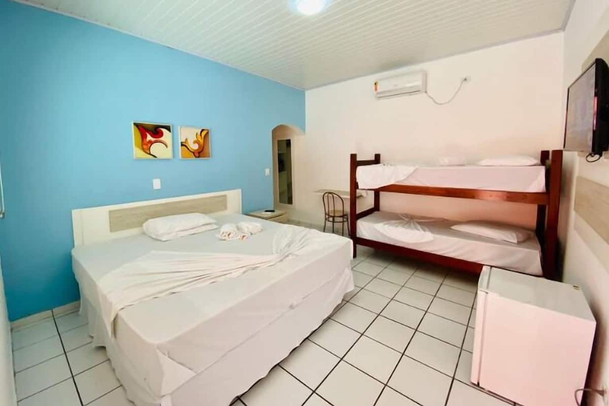 A hotel room with a large bed, a bunk bed, a small table, and a wall-mounted air conditioner.