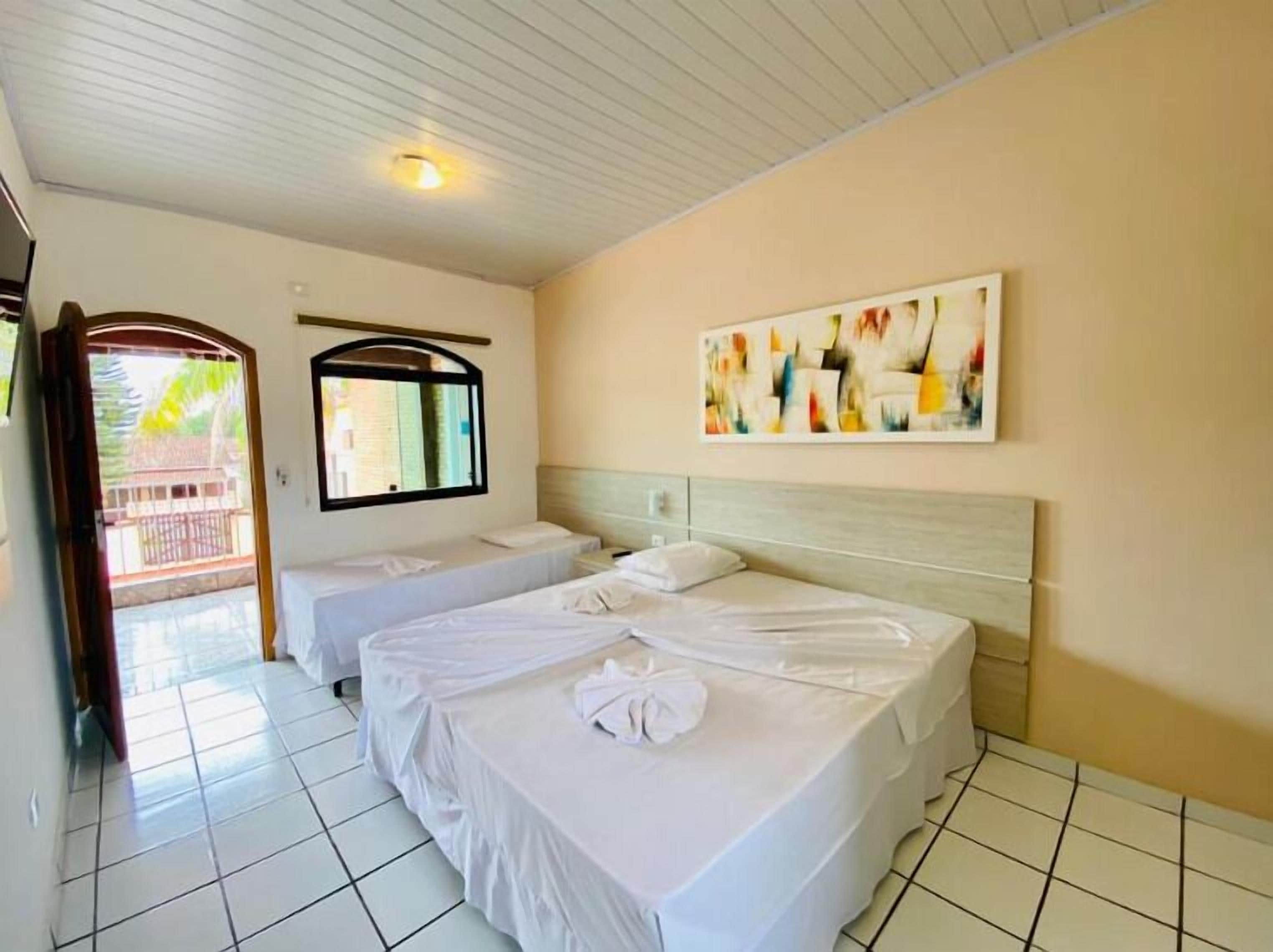 A hotel room with two beds, a large window, a ceiling light, and a colorful abstract painting.