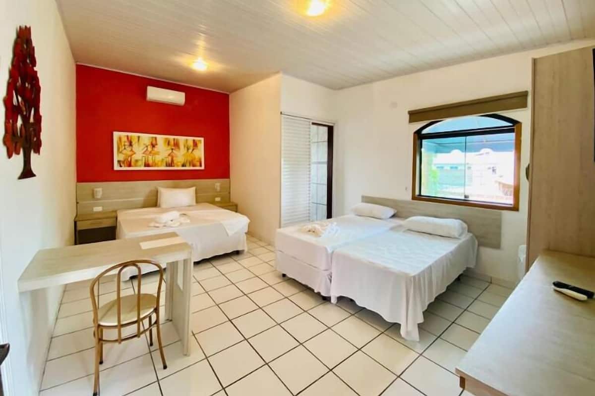 A hotel room with two beds, a desk, a chair, and a window with a view.