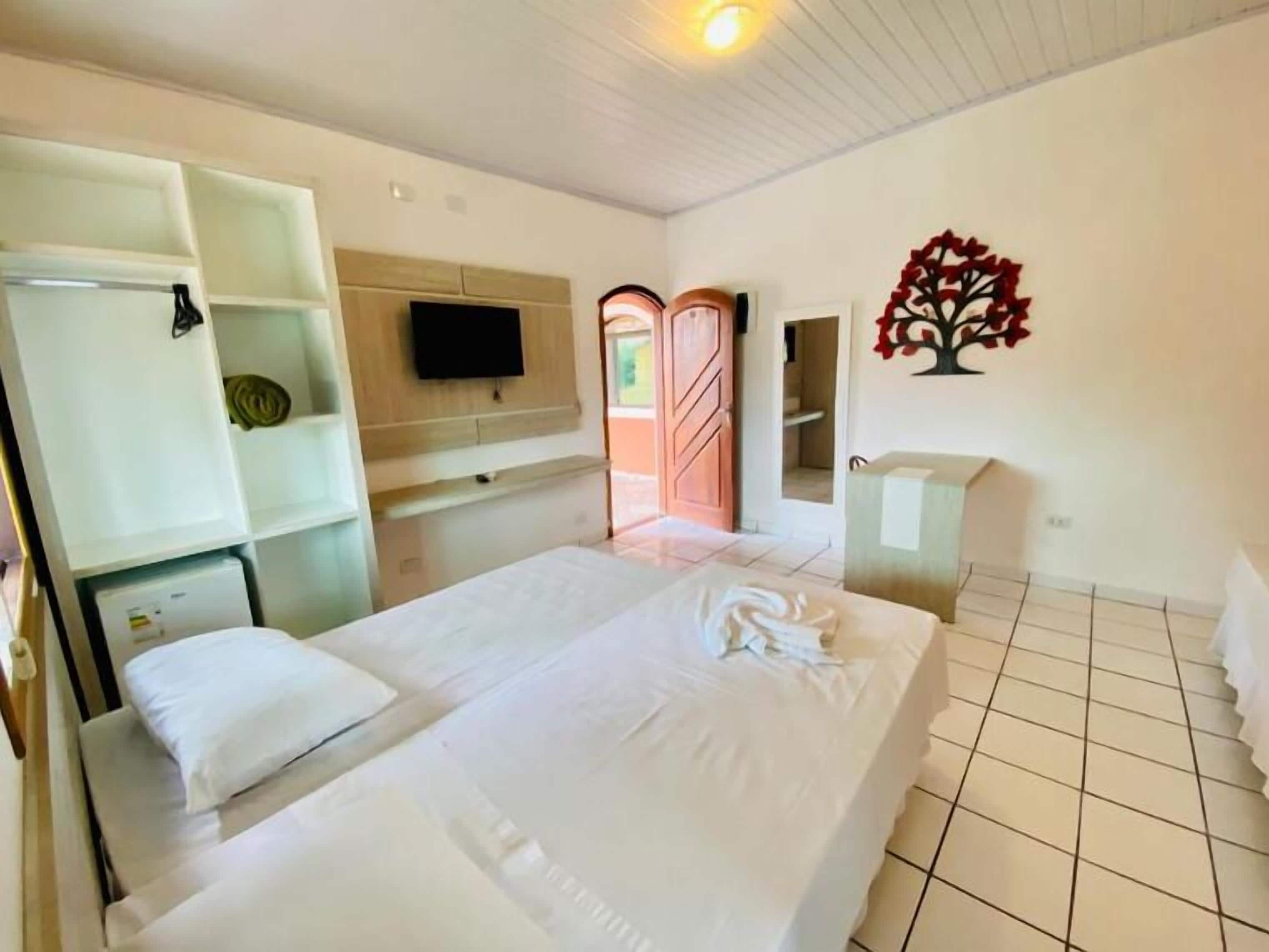 Quarto de hotel com uma cama, televisão na parede, área de chuveiro e um pequeno armário.
