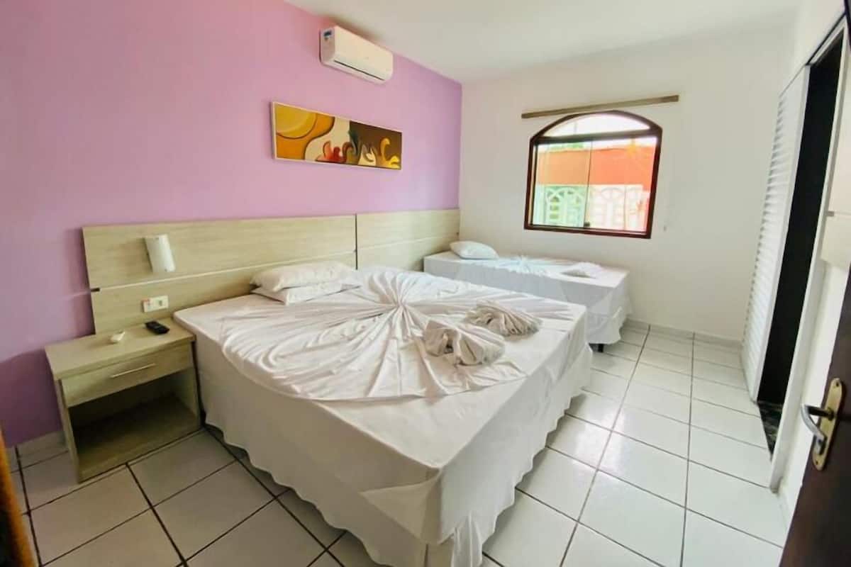 A hotel room with a large bed, a smaller bed, a nightstand, a window with a view, and a wall-mounted air conditioner.