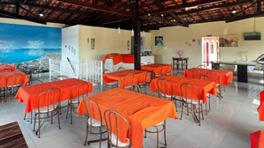 A restaurant with multiple tables covered in orange tablecloths, a tiled floor, and a wooden ceiling structure. - Pousada Porto do Rio Praia (Caraguatatuba)