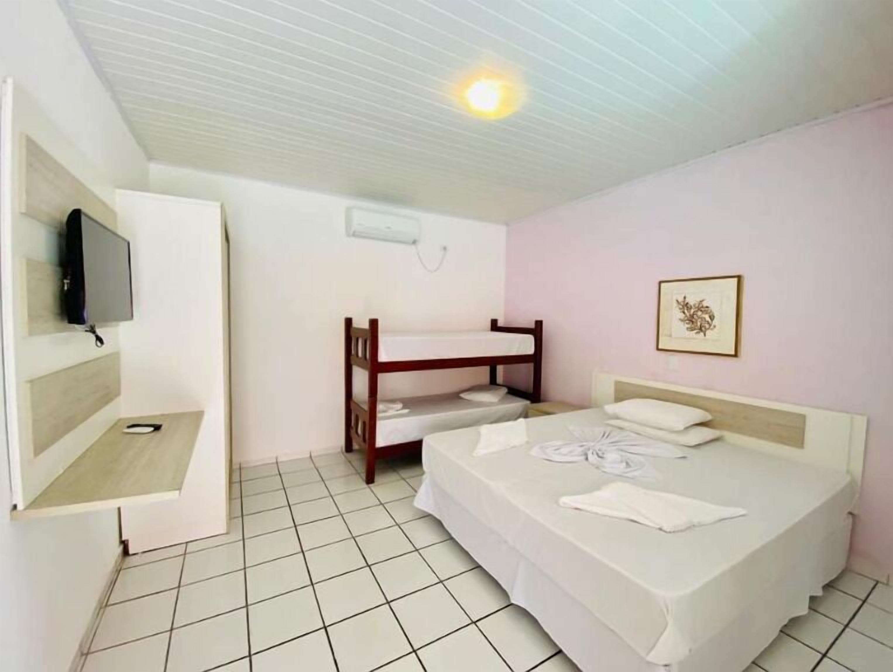 Ein Schlafzimmer mit Etagenbett, einem Einzelbett, einem flachbildfernseher an der Wand und einem kleinen Nachttisch.