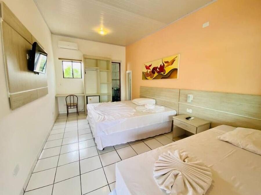 A hotel room with two beds, a television mounted on the wall, a chair, and a painting on the wall.