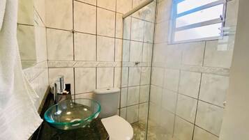 Un baño con lavabo de cristal, inodoro y zona de ducha.