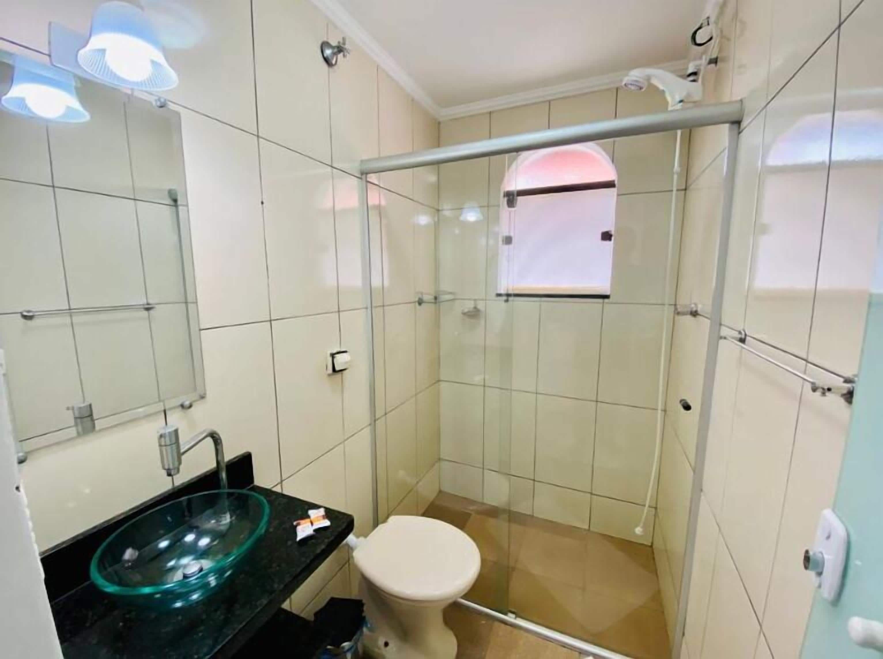 Un baño con cabina de ducha de vidrio, lavamanos de vidrio y un inodoro.