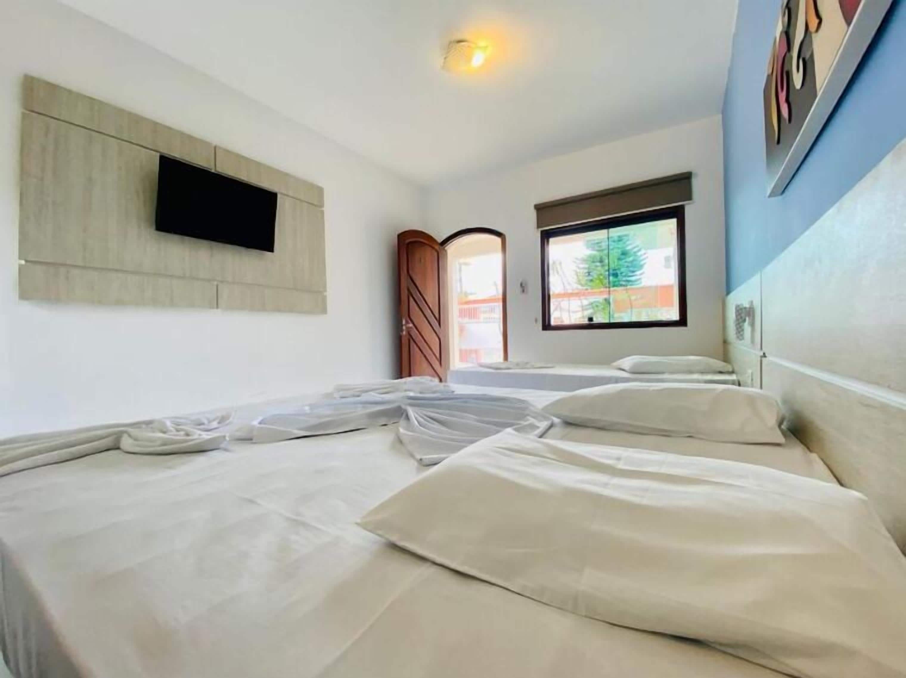 A hotel room with a bed, a TV mounted on the wall, a window with a view of the outside, and a door leading to another room.