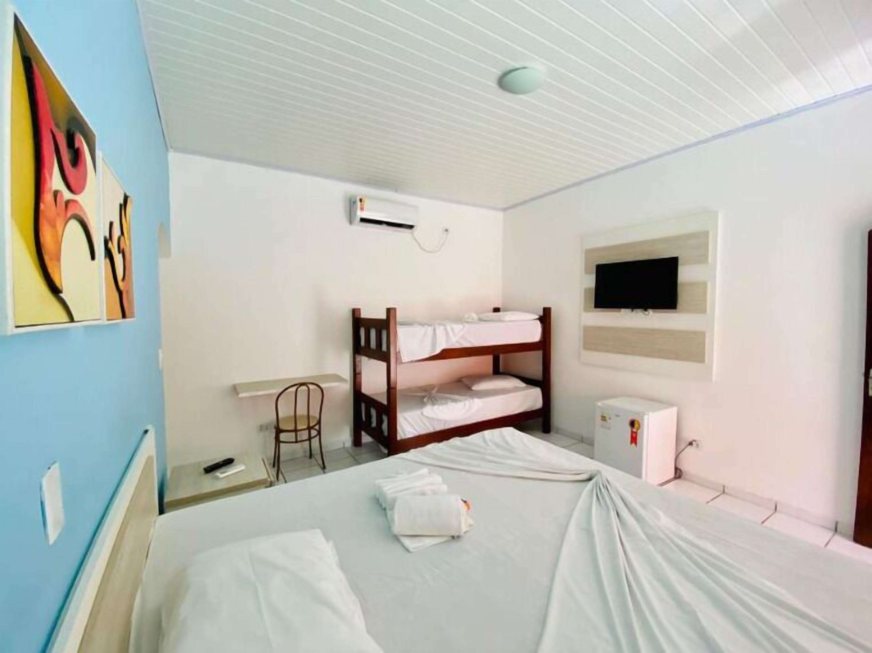 A room with bunk beds, a desk, a chair, a TV, and an air conditioning unit.