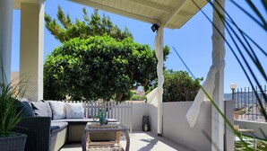 Eine überdachte Terrasse mit einem Rattansofa, einem kleinen Tisch und einem Topfpflanzen.