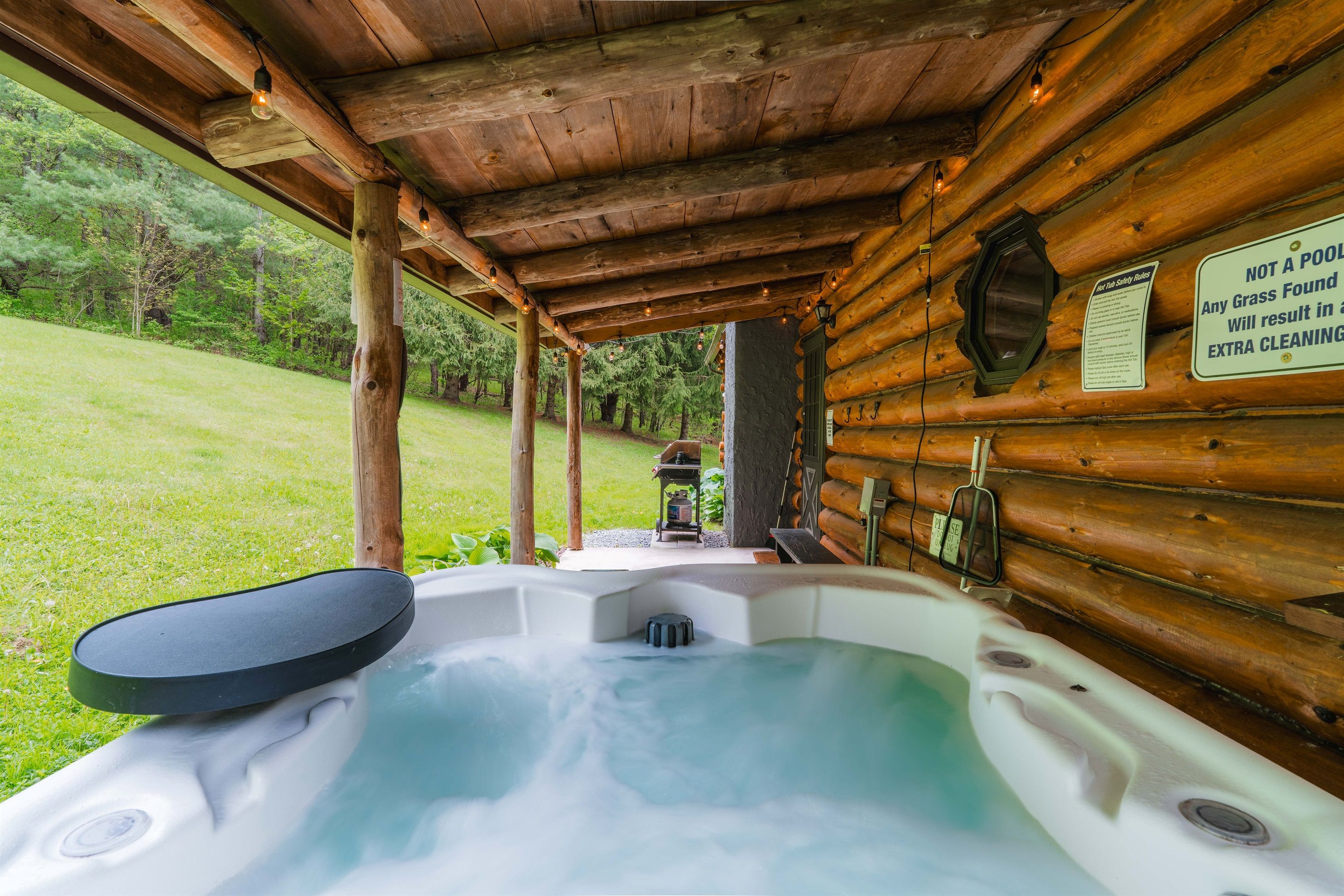 A hot tub under a wooden gazebo with a sign about grass and cleaning.