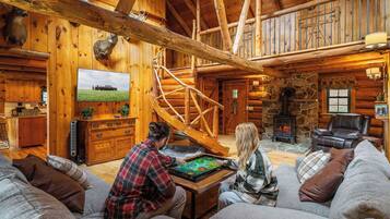 A cozy log cabin interior with a fireplace, wooden walls, and a staircase.