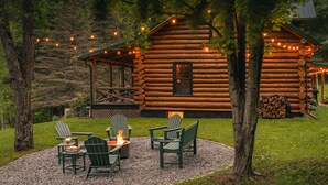 Hirsimökki, jonka pihalla on nuotiopaikka ja Adirondack-tyyliset puutarhatuolit.
