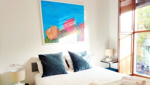 Quarto de hotel com uma cama grande, duas almofadas, mesa de cabeceira com abajur e janela com vista para árvores.