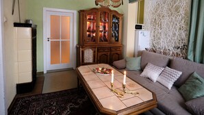 Een woonkamer met een bank, een bijzettafeltje met kaarsen, een houten kast en een behang met patroon.