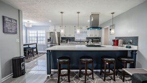 A modern kitchen with a large island, bar stools, stainless steel appliances, and pendant lighting. - Super Luxurious House (Atlanta)