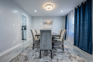 A dining area with a marble floor, a chandelier, a painting on the wall, and a view of the kitchen.