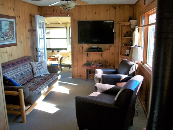 A cozy cabin interior with a wooden interior, a sofa, a chair, a television, and a window. - Cozy 2 Bedroom Cabin With Gas Fireplace (Saint Germain)