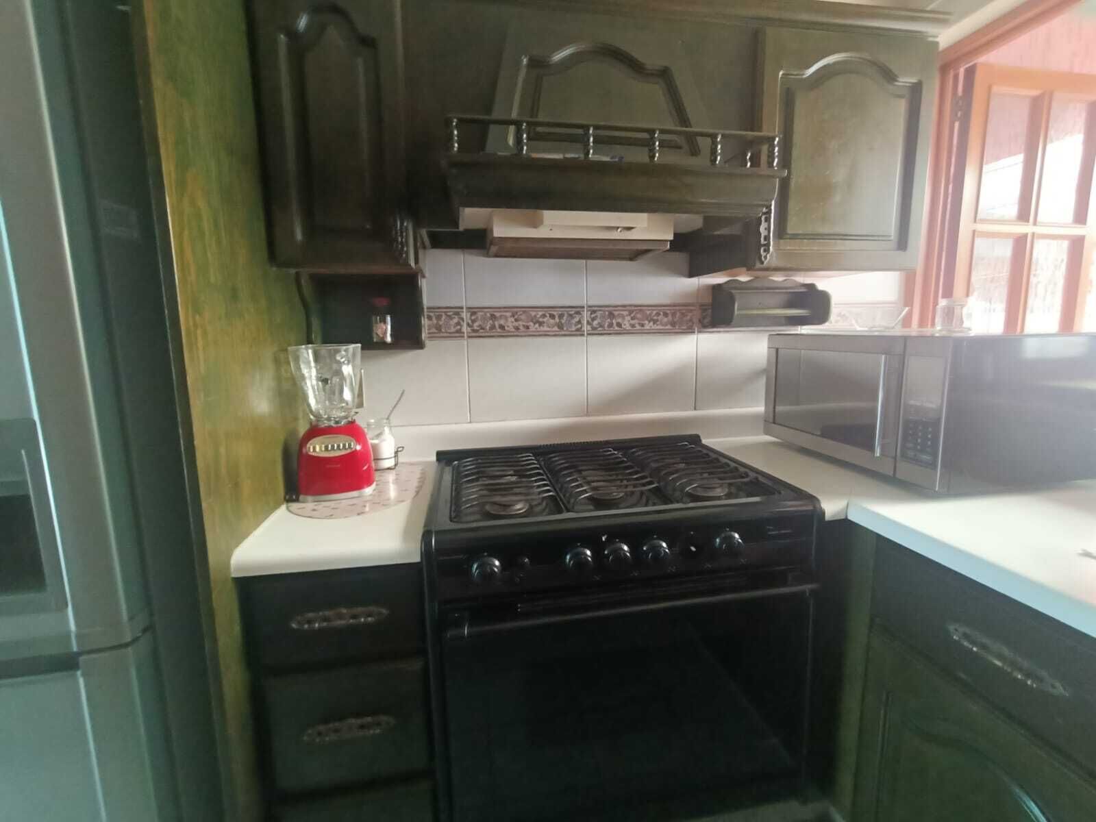 A kitchen with a gas stove, a microwave, and a red blender on the counter.