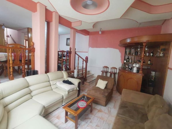 A living room with a beige sofa, a brown armchair, a wooden coffee table, and a bar area with bottles.