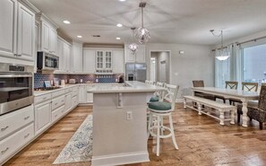 A modern kitchen with white cabinetry, a central island, and a dining area with a bench and chairs.