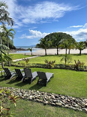 Un área de descanso junto a la playa con sillones, un césped y vista al océano.