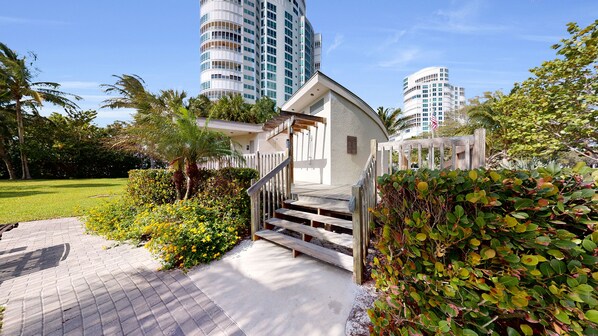 A residential building with a staircase leading to a door, surrounded by lush greenery and palm trees.