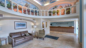 Un hall d’entrée spacieux avec un plafond haut, un comptoir de réception portant l’inscription « CAMELOT », un canapé en cuir marron et une petite table ronde.