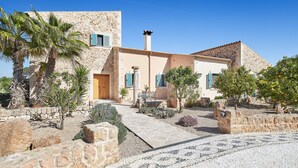 Une villa de style méditerranéen avec une façade en pierre, une cour intérieure aménagée avec des sièges et des palmiers.