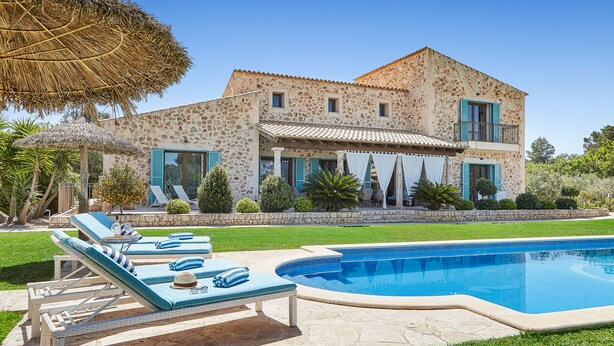 Une maison en pierre avec une piscine, des chaises longues et un parasol en chaume.