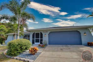 A single-story house with a blue garage door, a front entrance, and a well-maintained lawn with various plants.